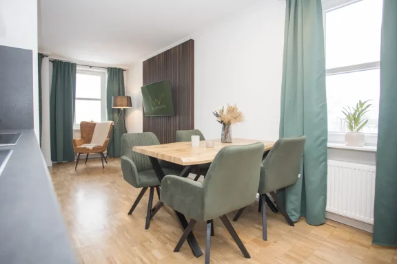 Moderne woonkamer met een houten eetkamertafel en groene stoelen. Raam met groene gordijnen.